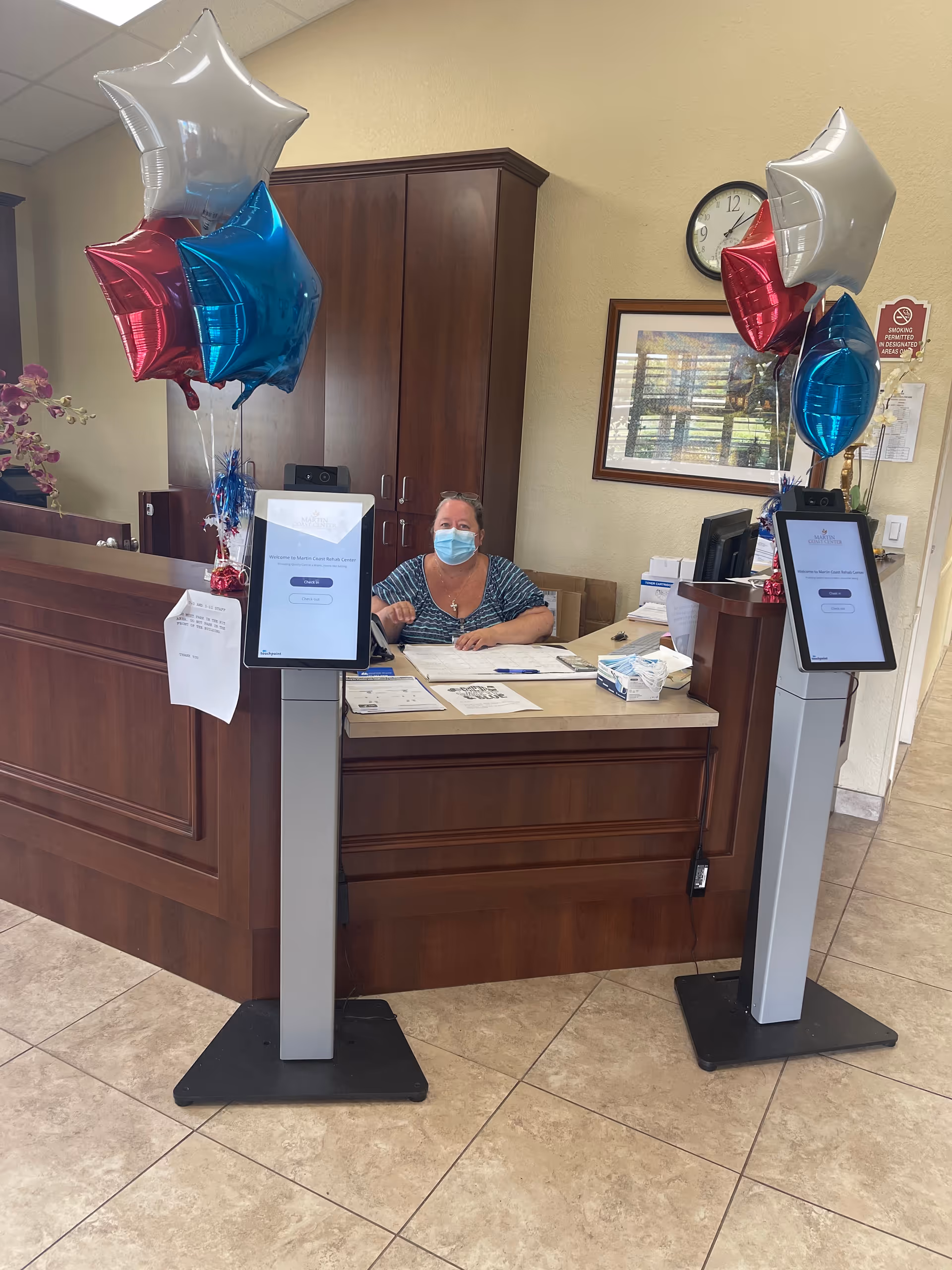 Reception desk in a Martin Coast Center lobby with balloons and a masked staff member.