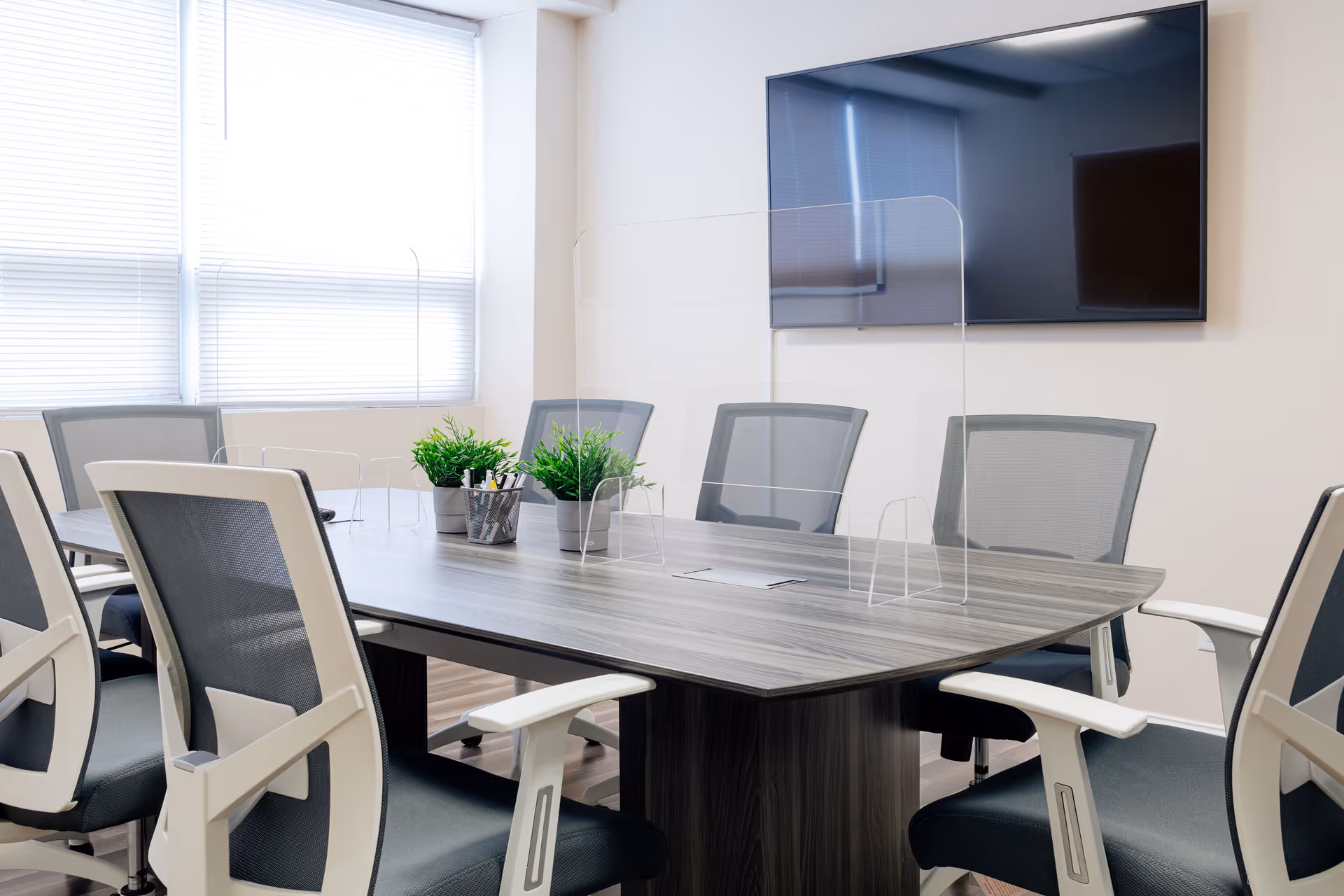 A modern conference room with a large table, chairs, and a wall-mounted TV.