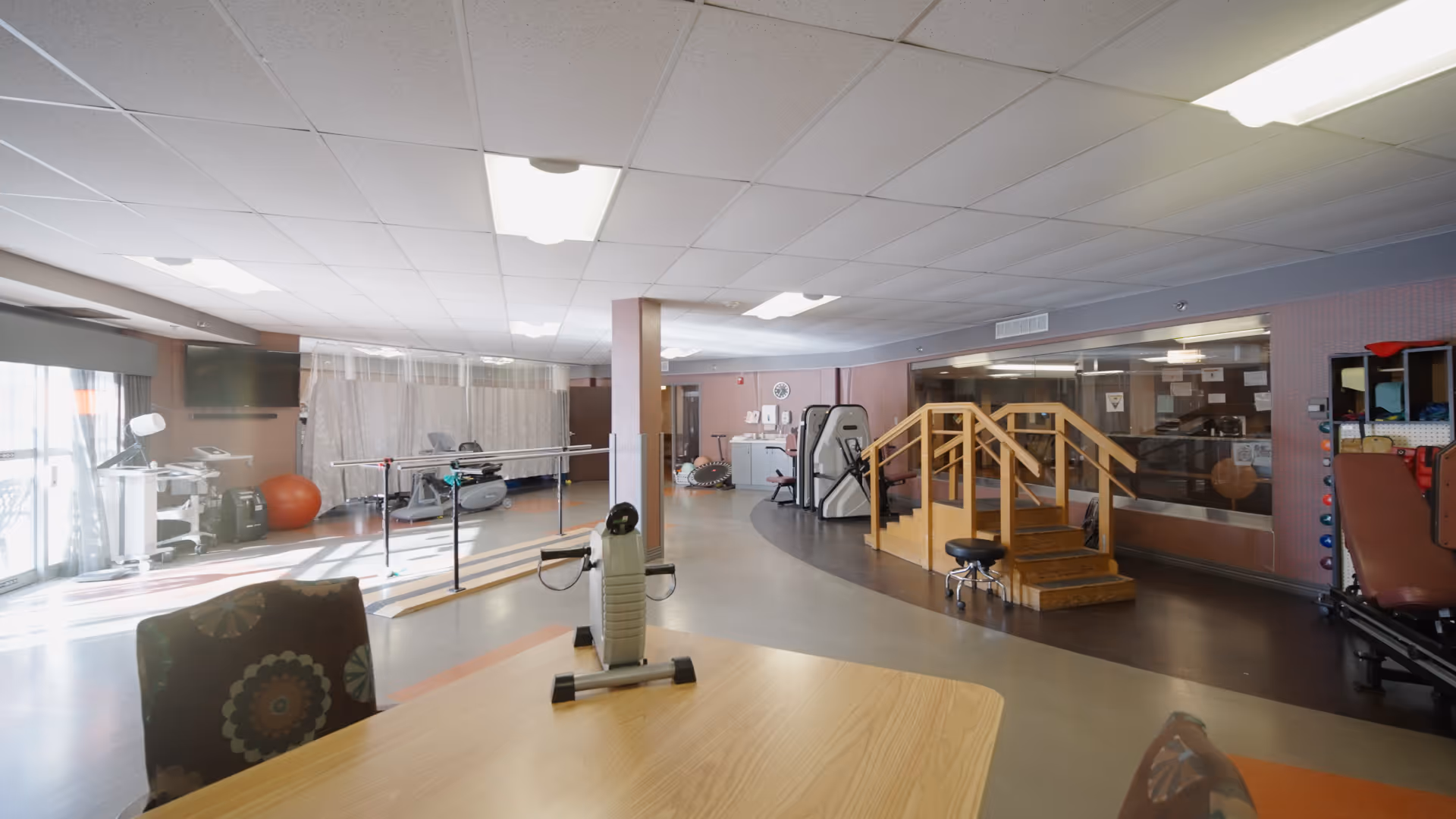 Indoor rehabilitation gym at Villa at Bradley Estates with exercise equipment and a wooden staircase.