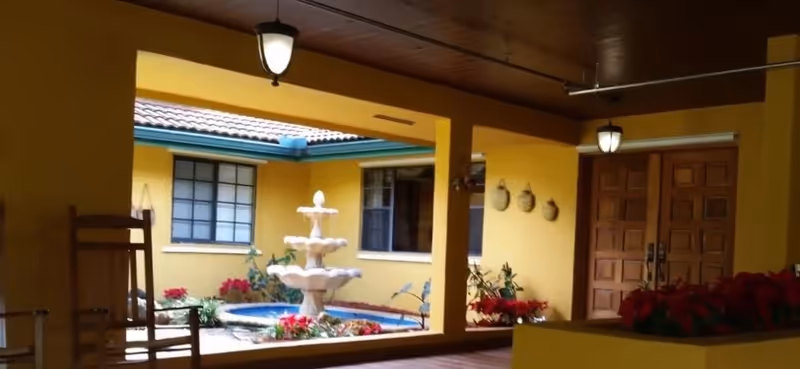 Covered interior courtyard with a tiered fountain, potted plants, yellow walls and wooden double doors.