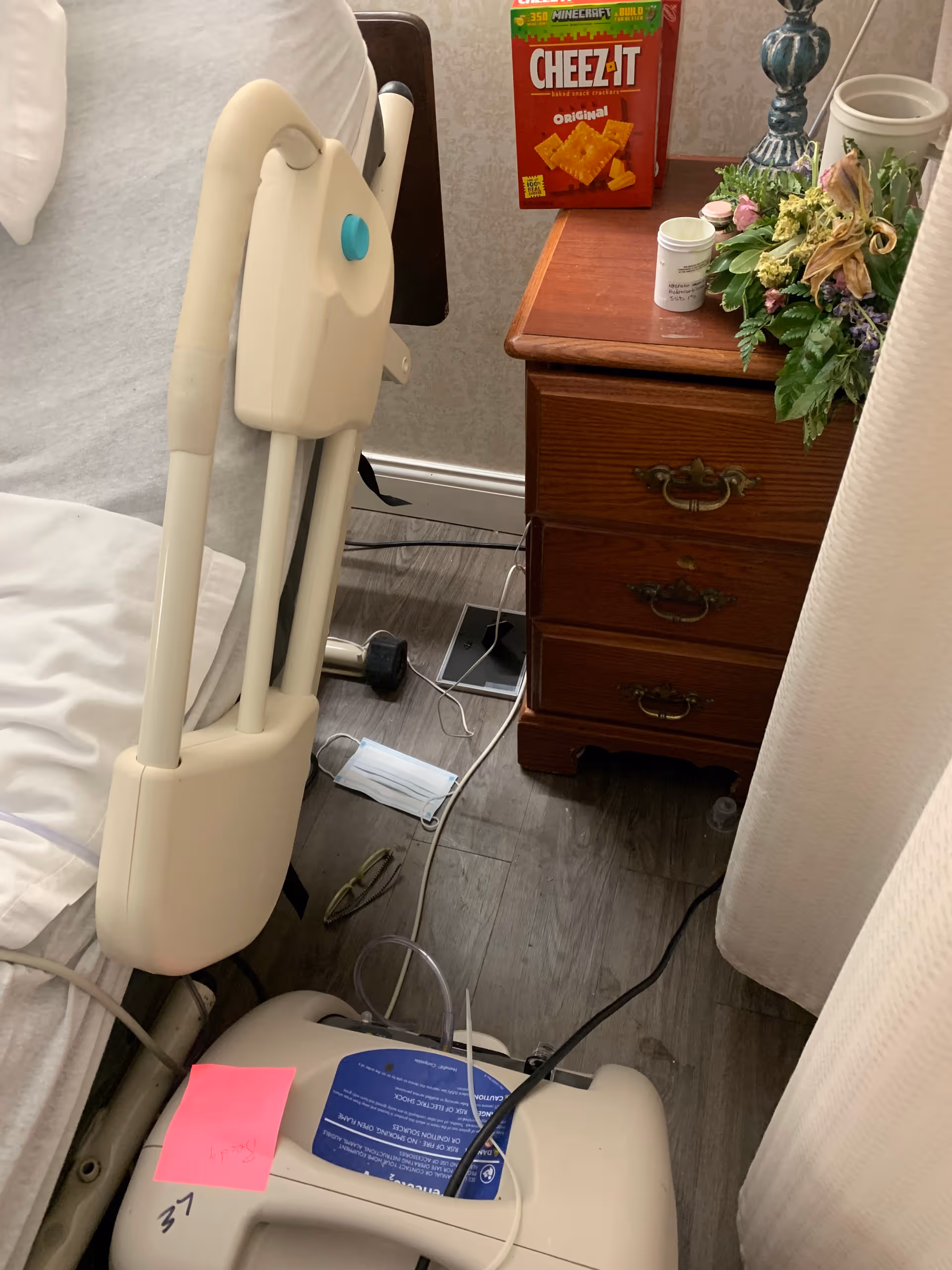 Hospital bed with side rails beside a wooden nightstand in a furnished bedroom.