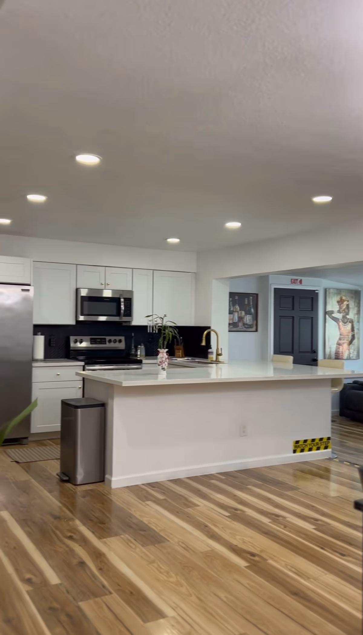 Bright modern kitchen with white cabinets, island, stainless appliances, and wood floors.