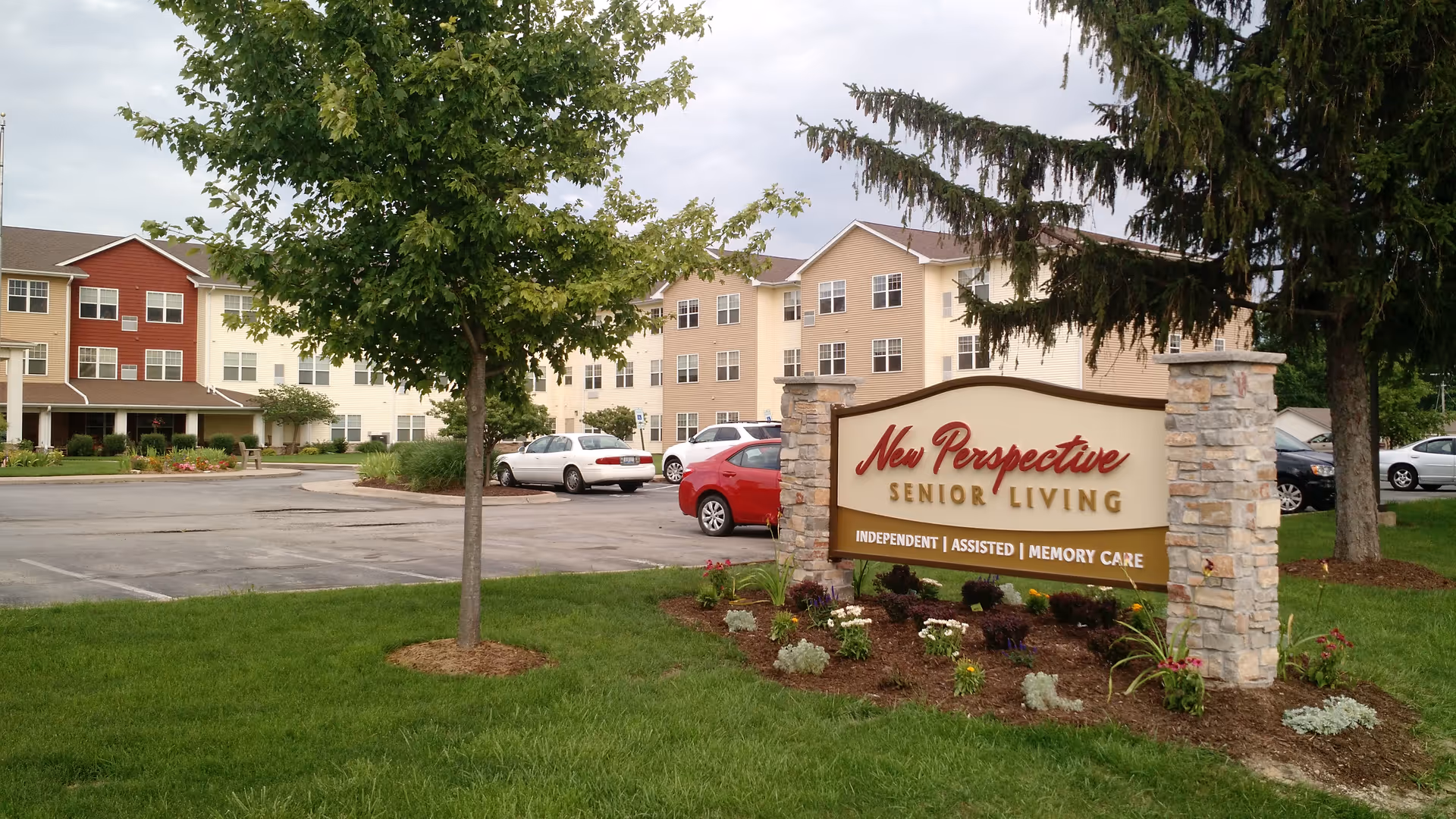 Exterior view of New Perspective Senior Living with sign, shrubs, and parked cars.