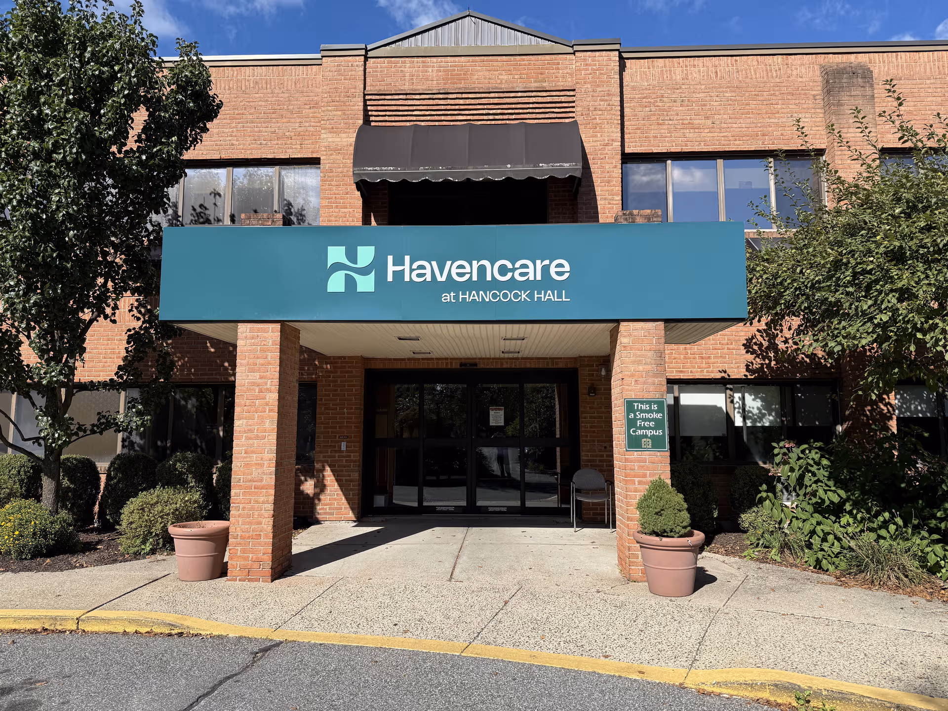 Brick senior living facility entrance with Havencare at Hancock Hall sign and glass doors.