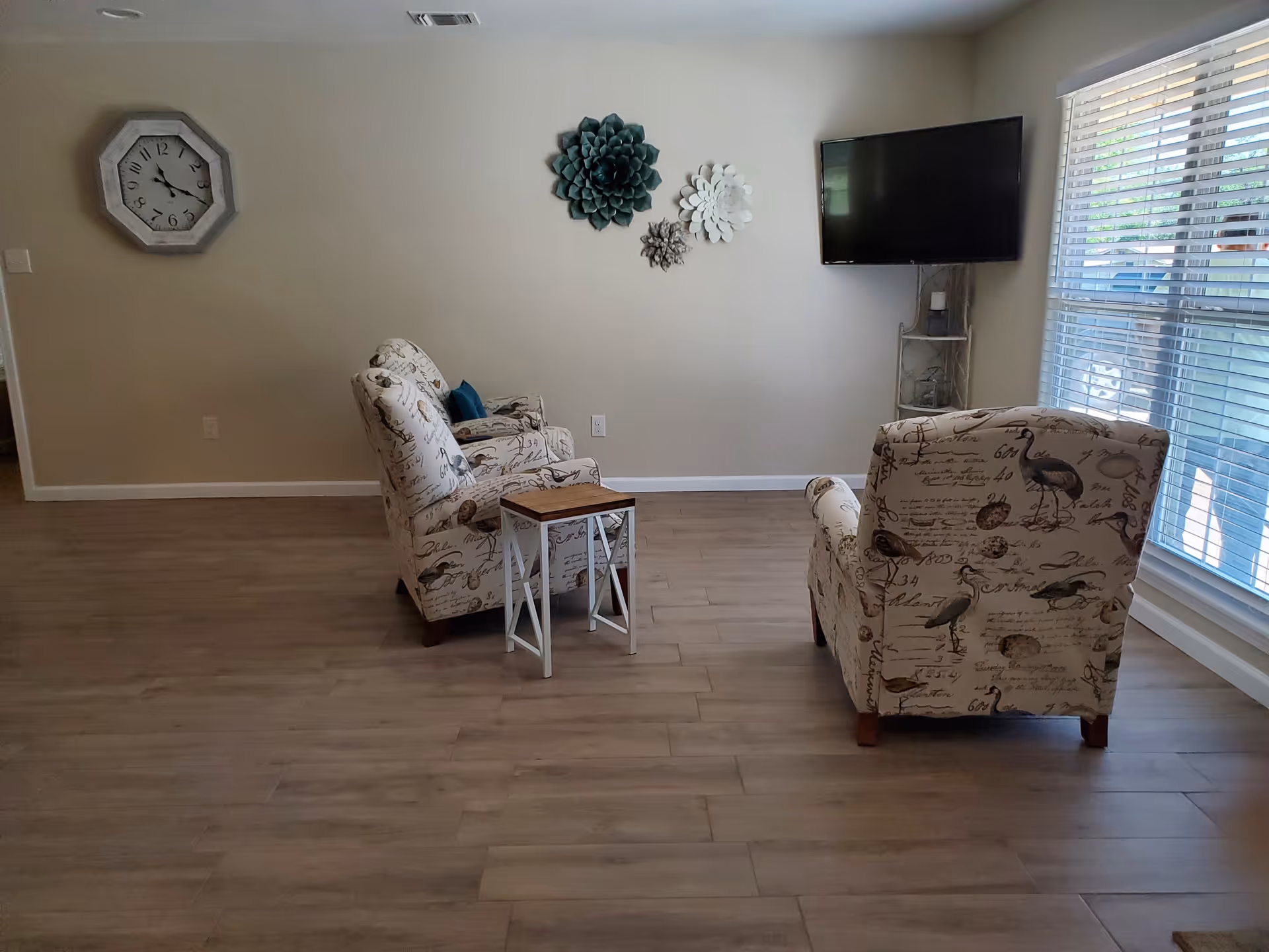 Two patterned armchairs face a wall-mounted TV in a bright living room.