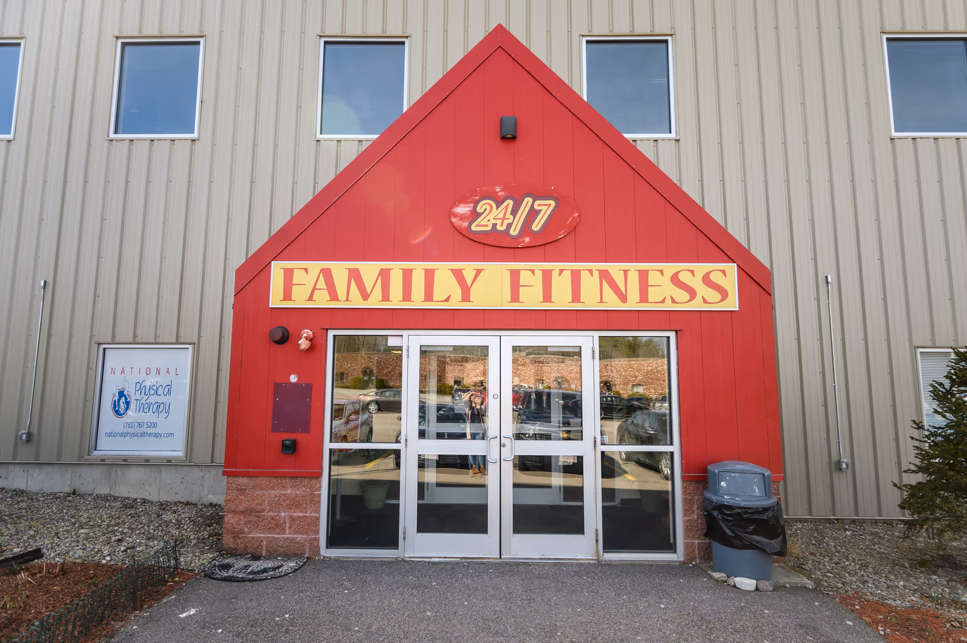 Front entrance of a building with a red Family Fitness sign and National Physical Therapy poster.
