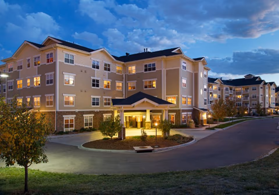 Exterior evening view of a multi-story senior living building with a lit main entrance and circular driveway.