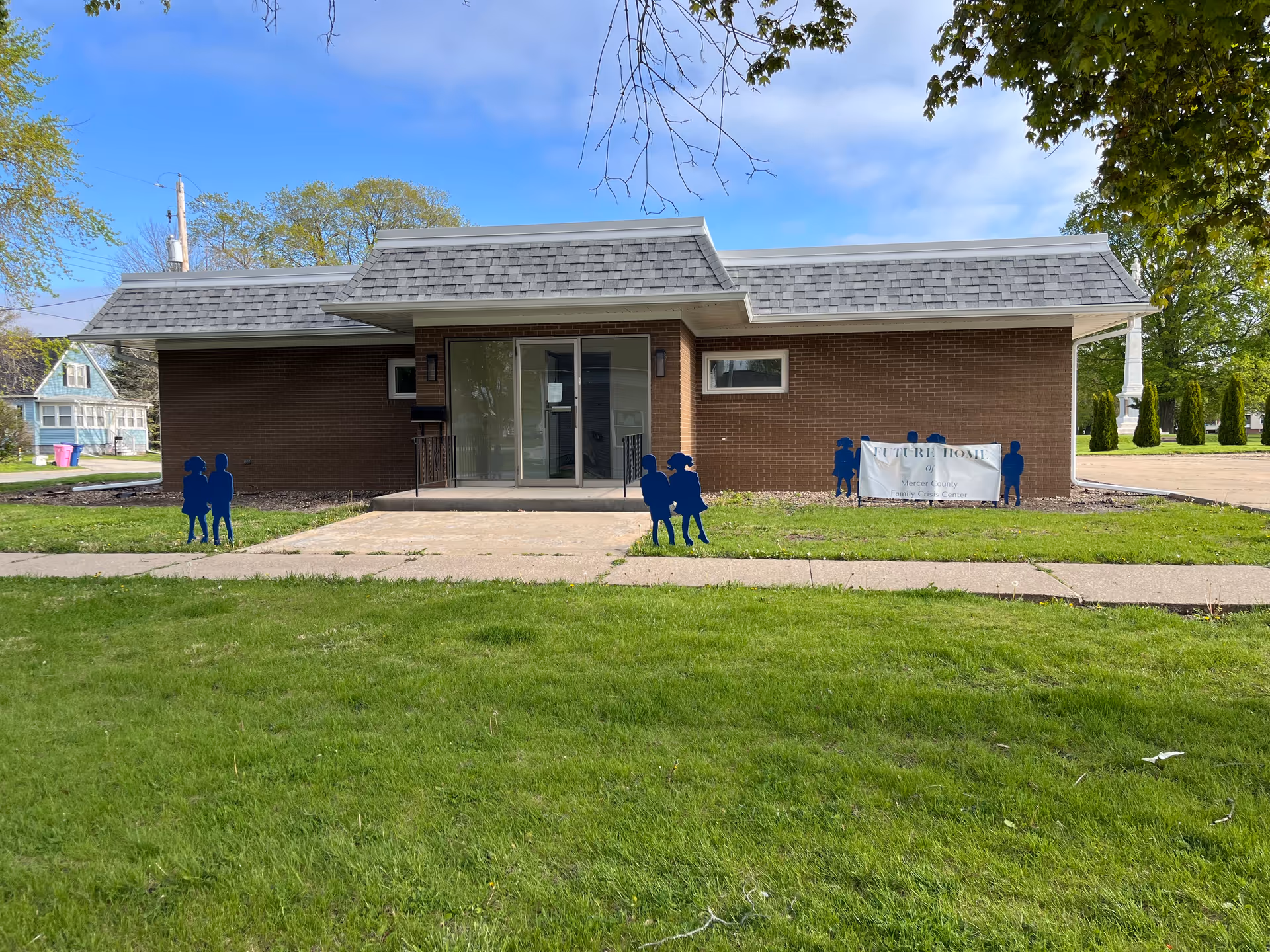 Brick one-story building with glass entrance and blue silhouette figures on the lawn.