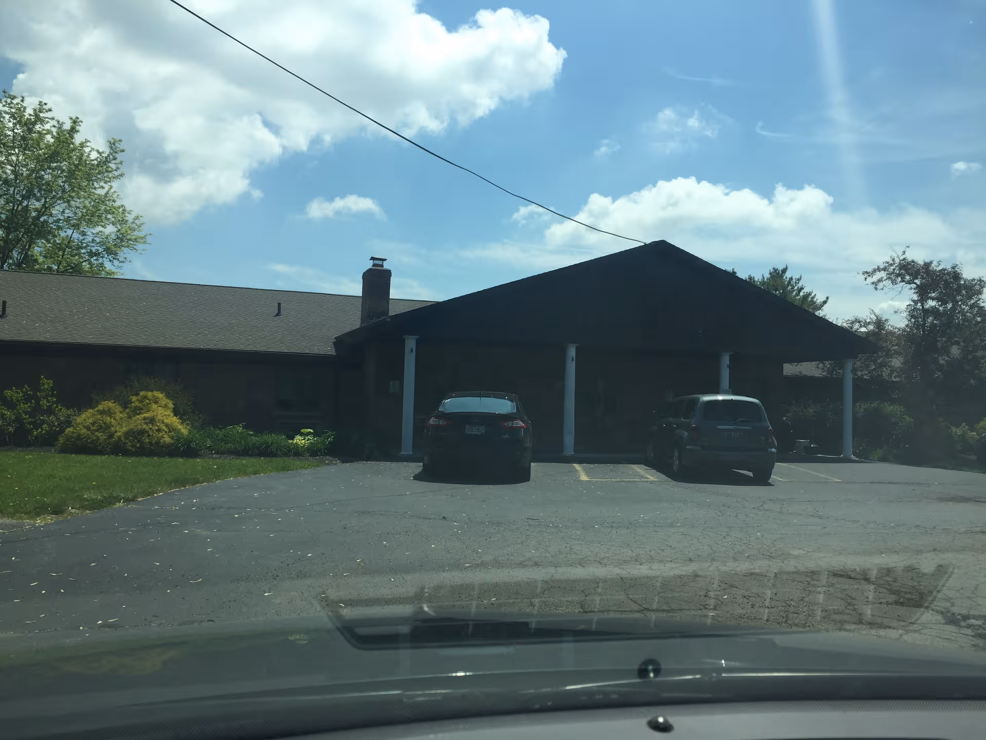 Front view of a low, single-story building with a covered entrance and parked cars.
