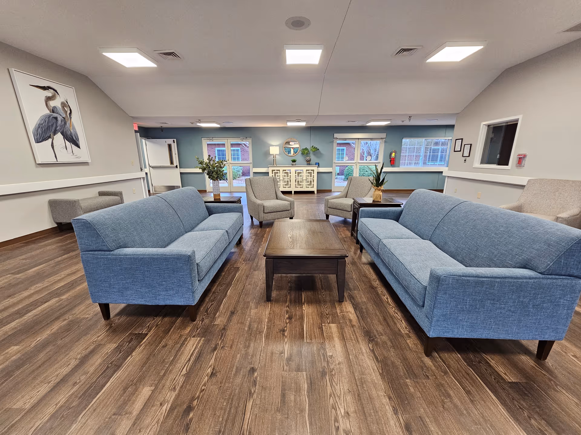 Spacious senior living lounge with blue sofas, coffee tables, and a reception desk.