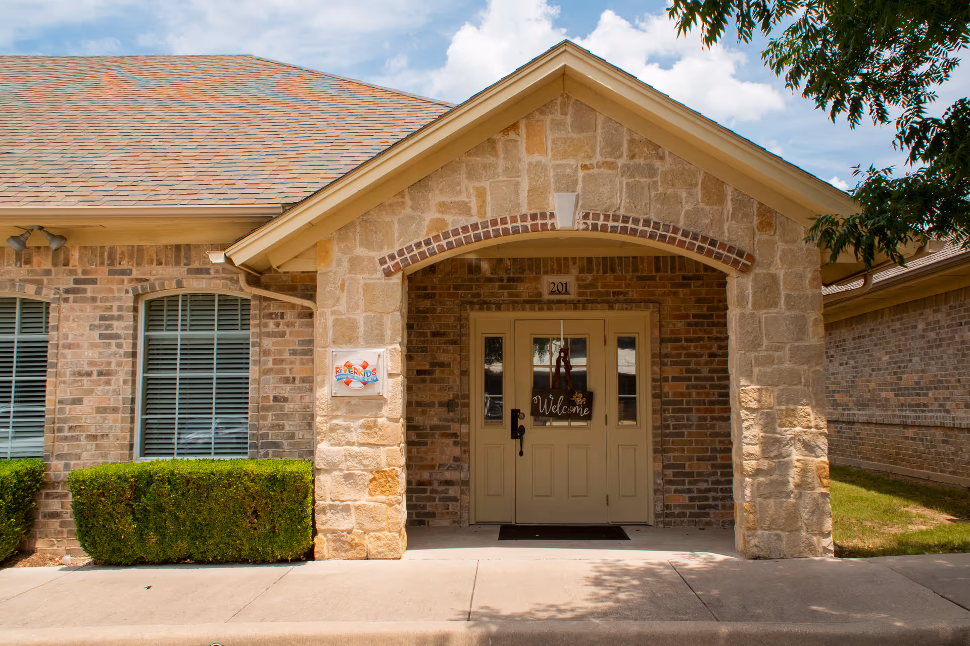 Stone building front with arched entry, double doors, and RiverKids sign beside.