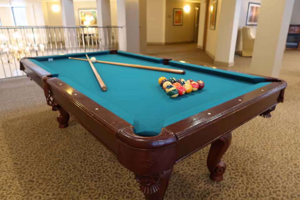 Indoor senior living lounge with a pool table, balls, and cues.