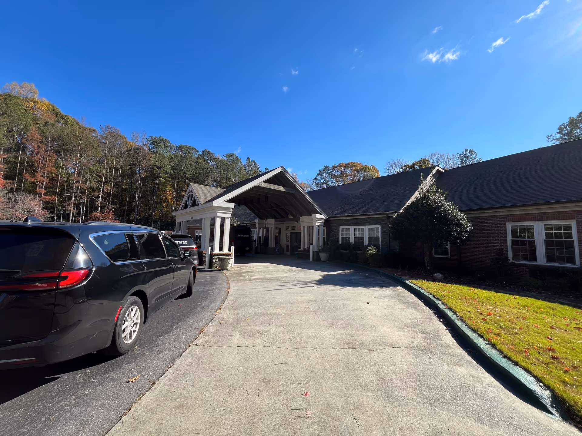 Senior living facility with a covered entrance, brick walls, and parked cars along a curved driveway.