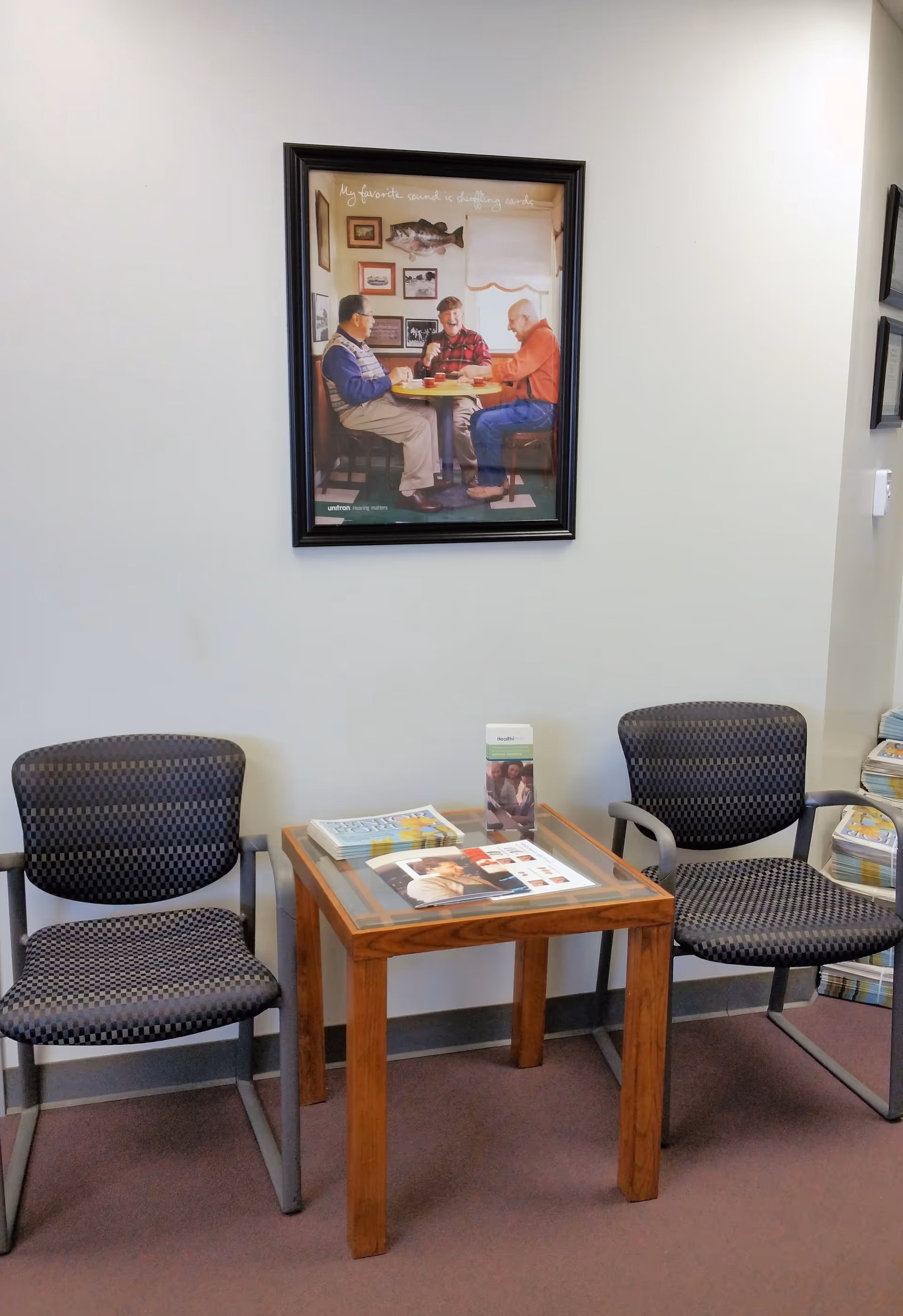 A small waiting area with two patterned chairs, a wooden table, and framed wall art.
