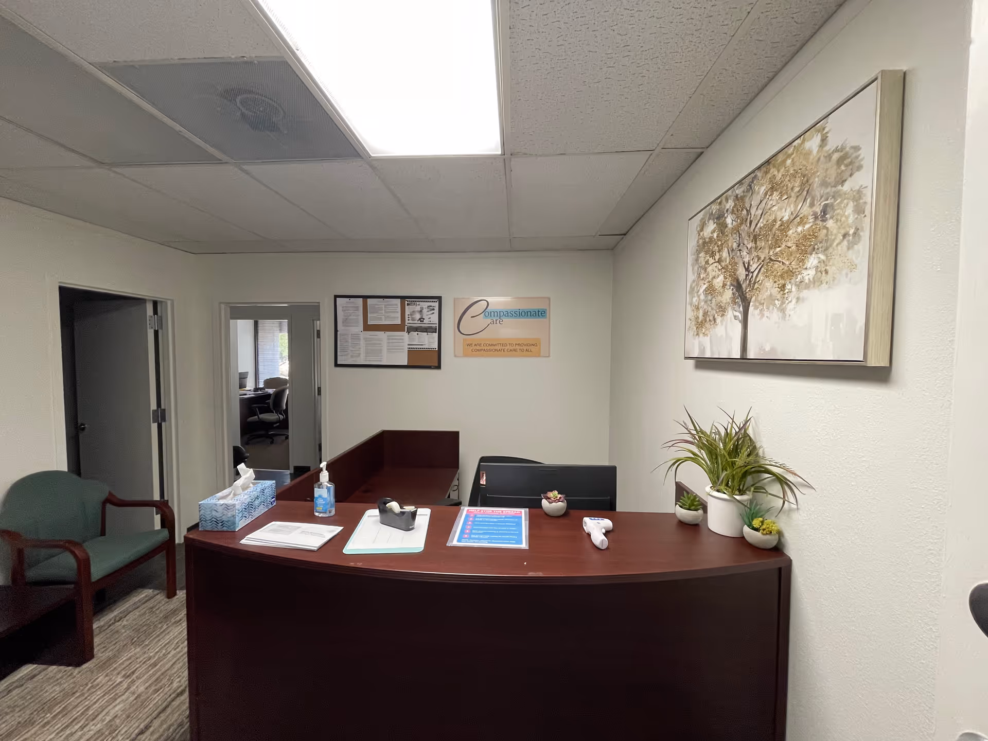 Reception desk in a quiet lobby with chairs, plants, and wall artwork.