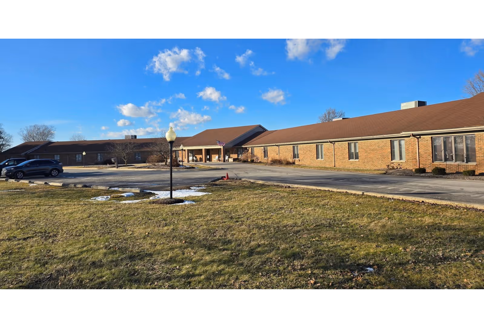 Exterior view of a long brick senior living facility with a parking lot.