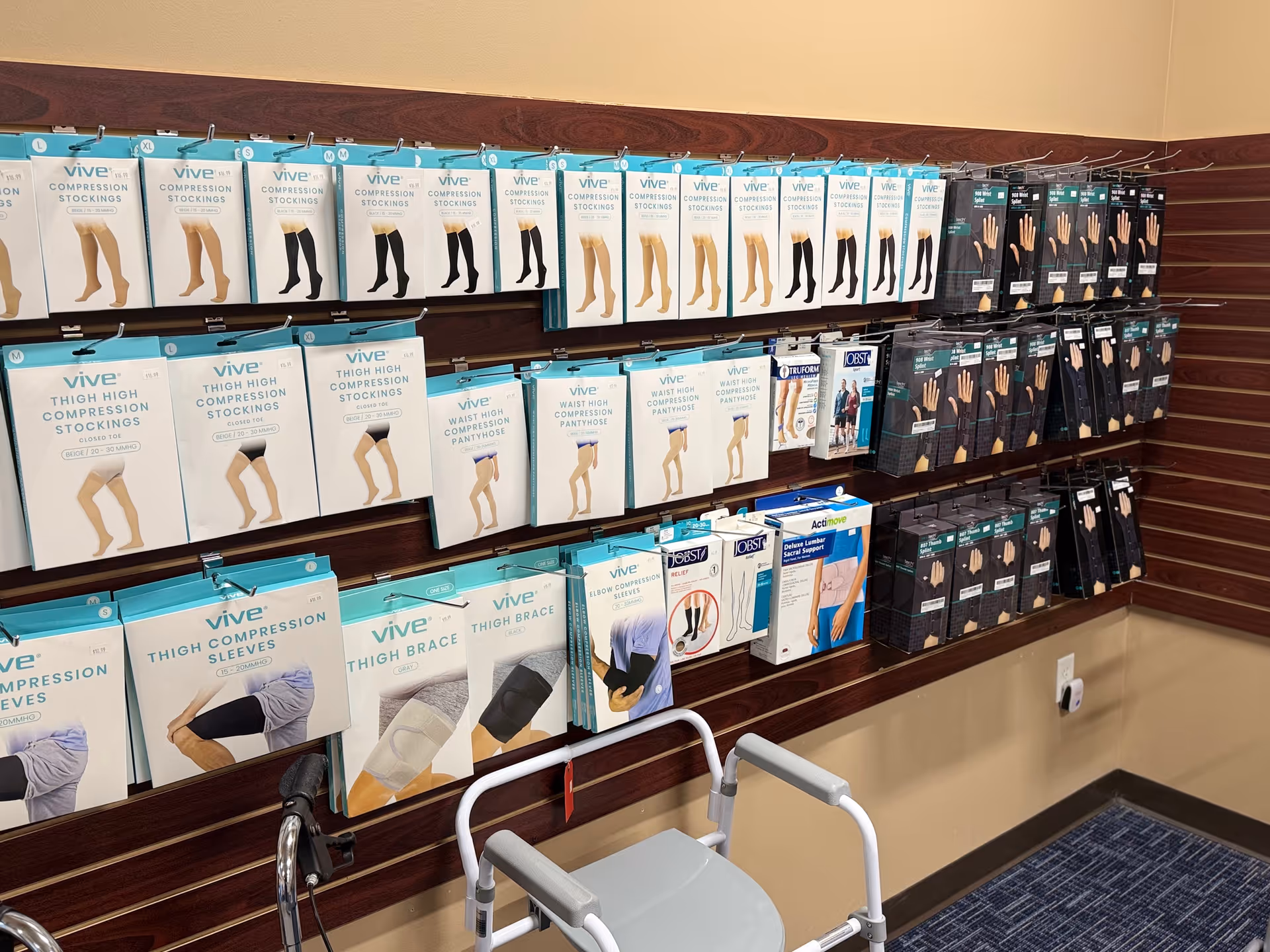 Indoor wall with stocked shelves displaying compression stockings and leg supports, with a walker in front.