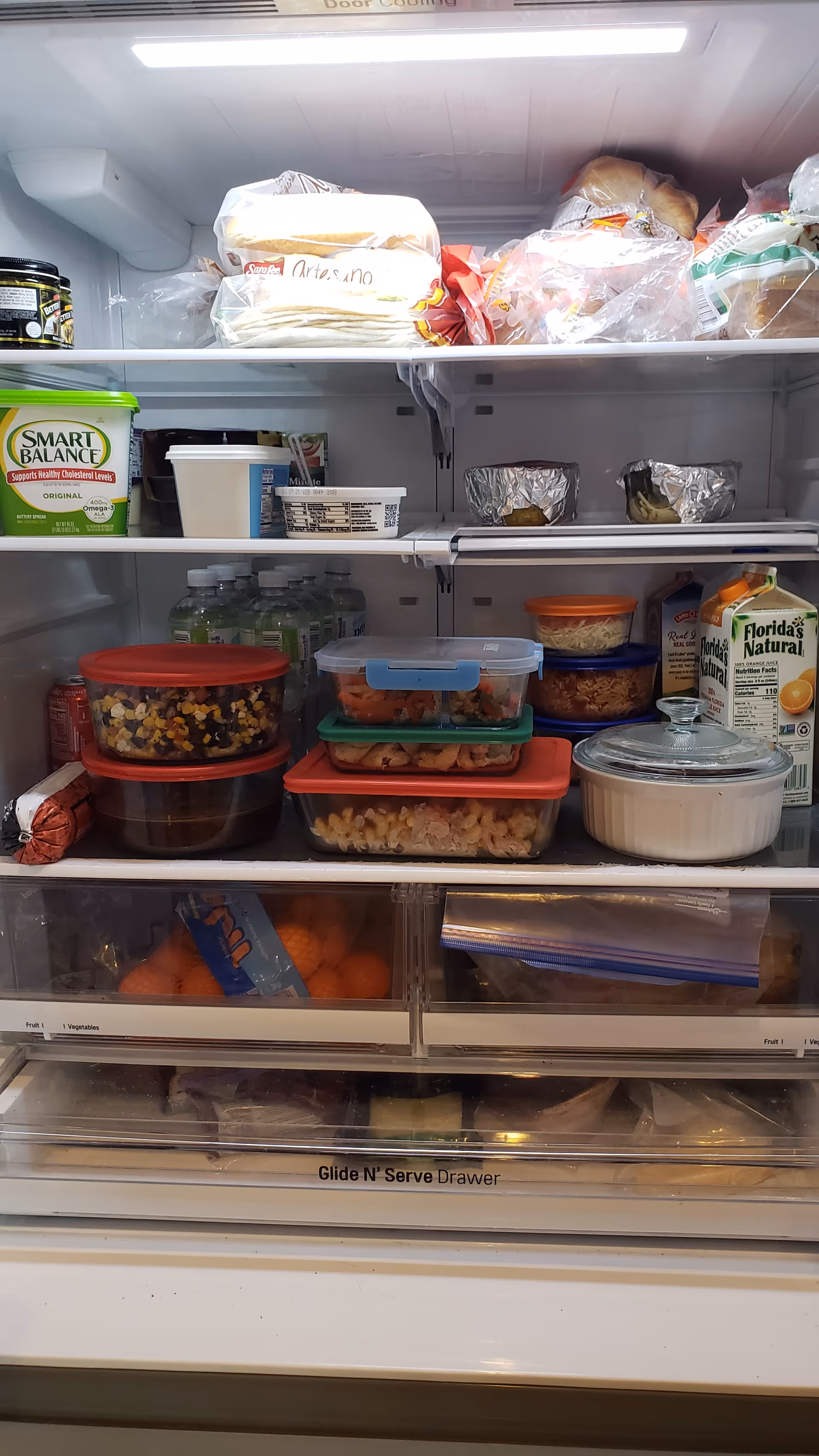 Open refrigerator filled with containers, bottles, and boxed foods on shelves.