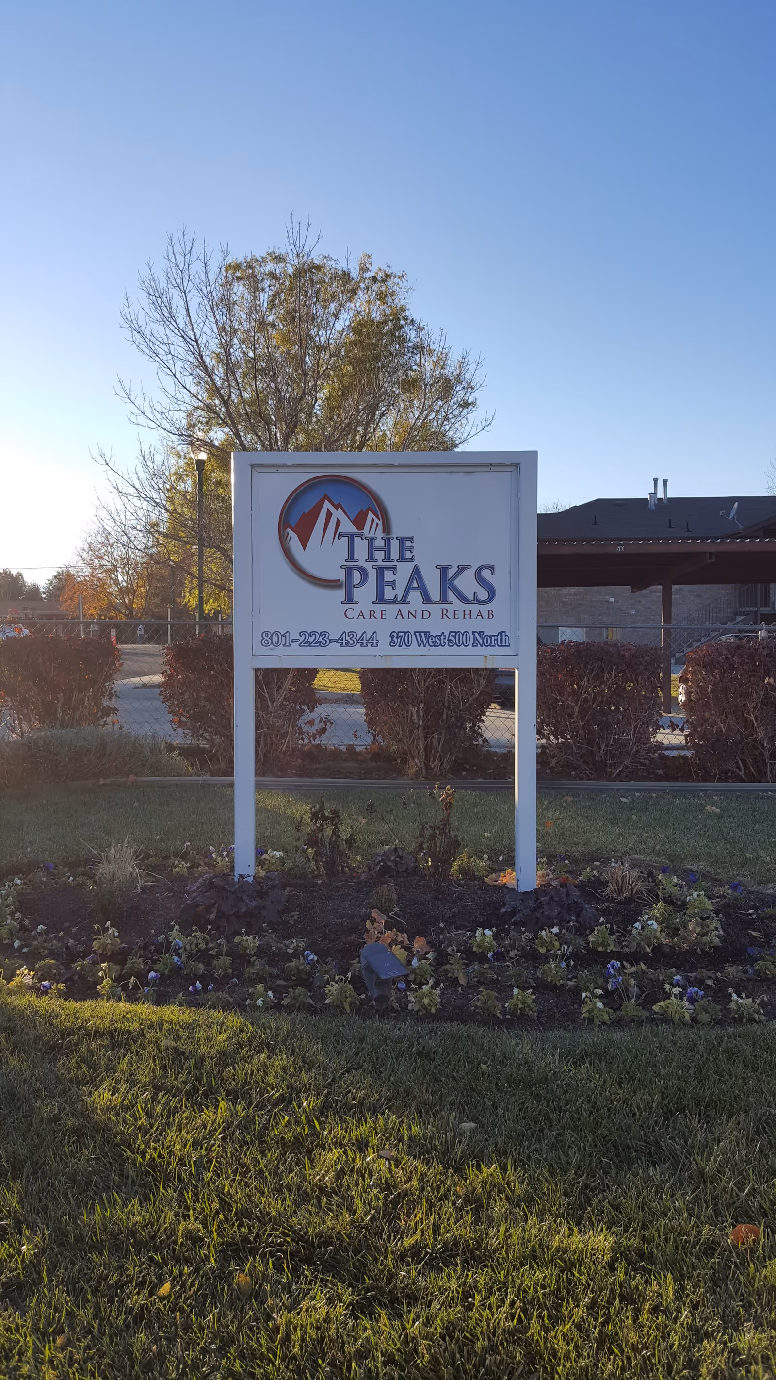 Front exterior sign reading The Peaks Care and Rehab with landscaping and clear blue sky.