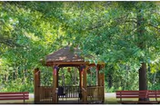 Wooden gazebo with benches in a green park-like outdoor area.