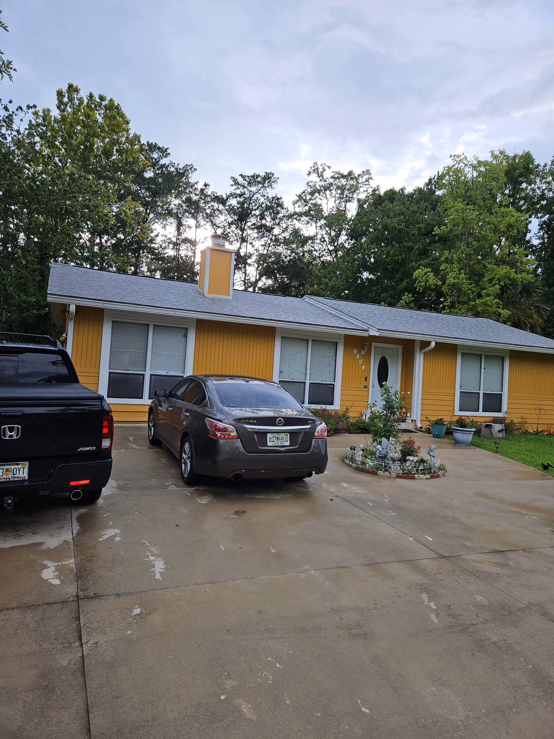 Yellow single-story facility facade with driveway, two cars, and small landscaped front garden.