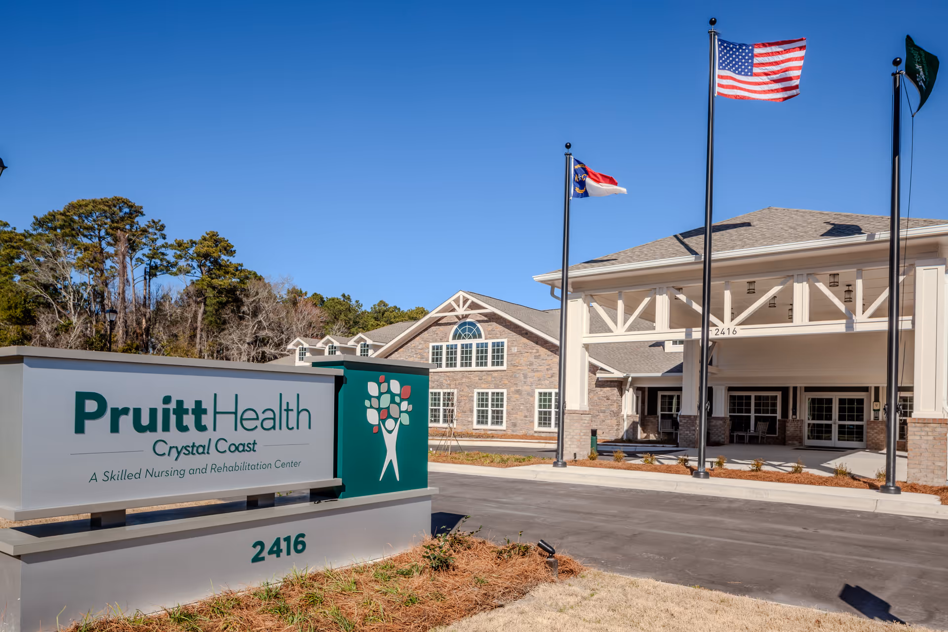 Exterior view of PruittHealth Crystal Coast facility with sign, entrance, and flags.