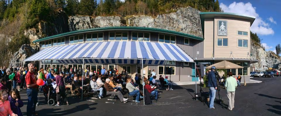 Exterior view of Community Connections facility with a striped awning and crowds gathered outdoors.