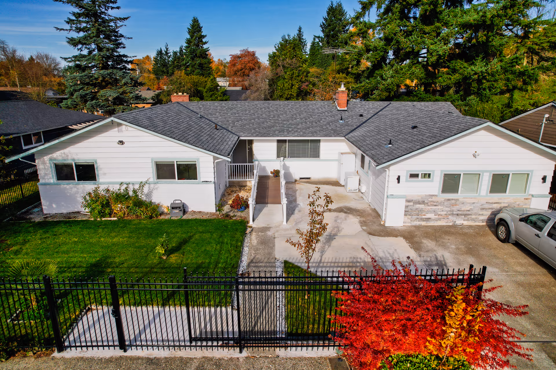 A single-story white senior living home with a black fence and autumn trees.
