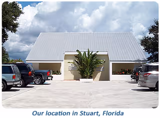 Light colored facility building front with parking lot and a large plant near entrance.