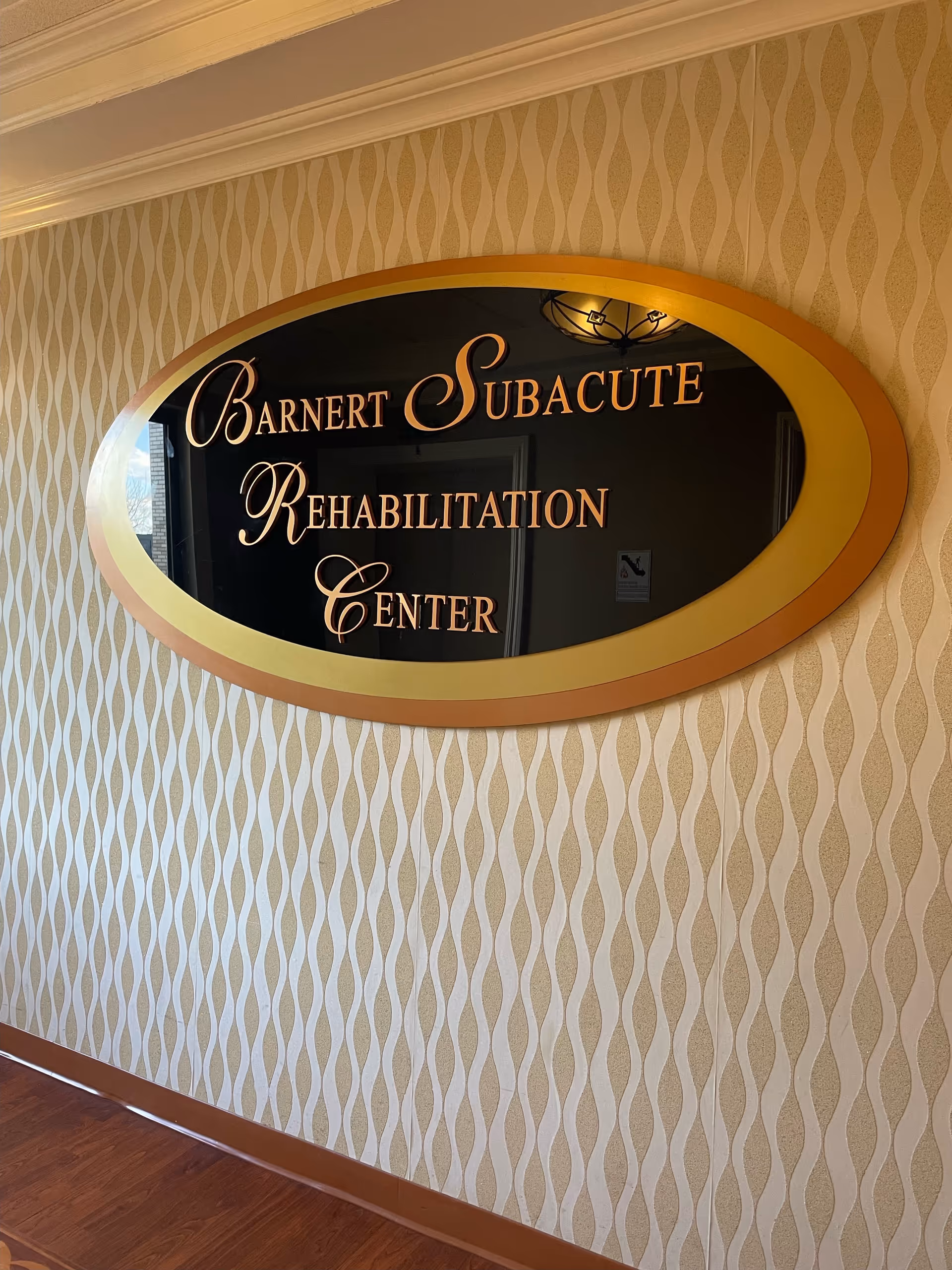 An oval gold-framed sign reading Barnert Subacute Rehabilitation Center is mounted on a patterned hallway wall.