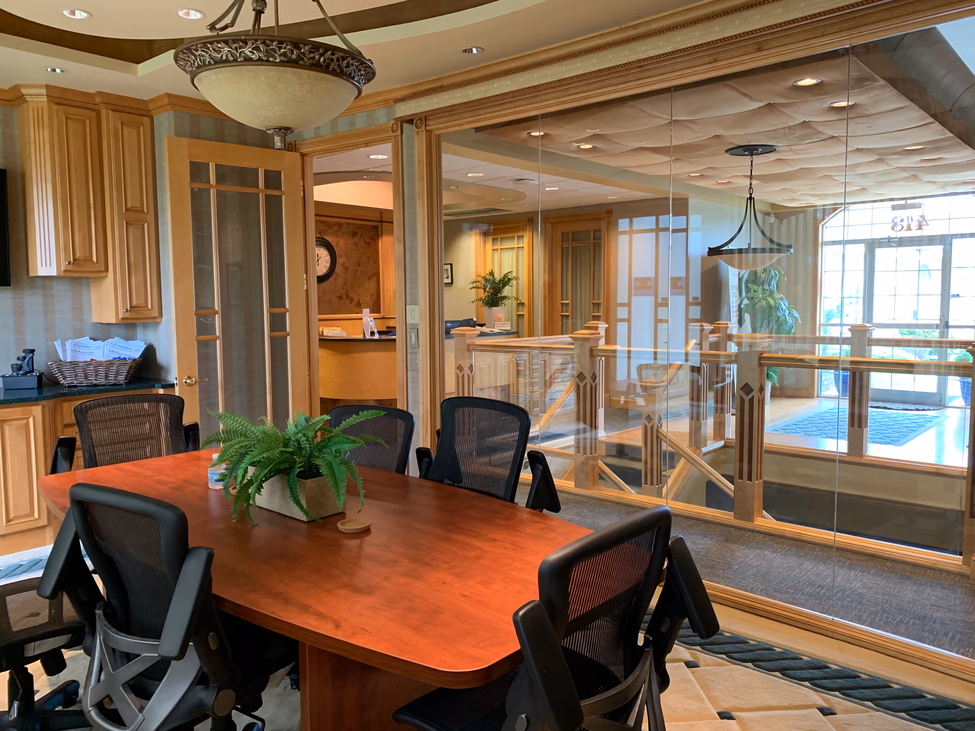 Interior dining area with a wooden table, black chairs, glass railing, and kitchenette.