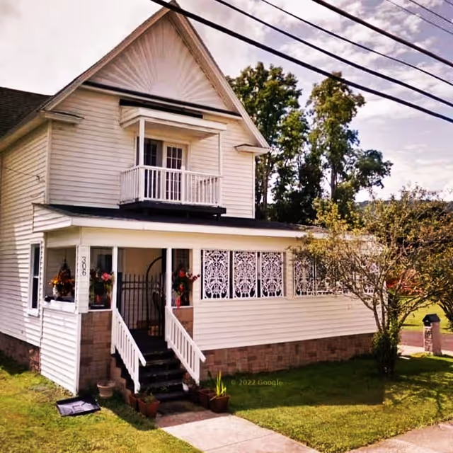 White two-story house with front porch, steps, and decorative lattice panels.