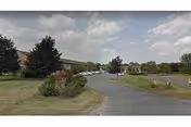 A curved driveway leads to Cabrini Acres Senior Apartment with manicured lawns and trees.