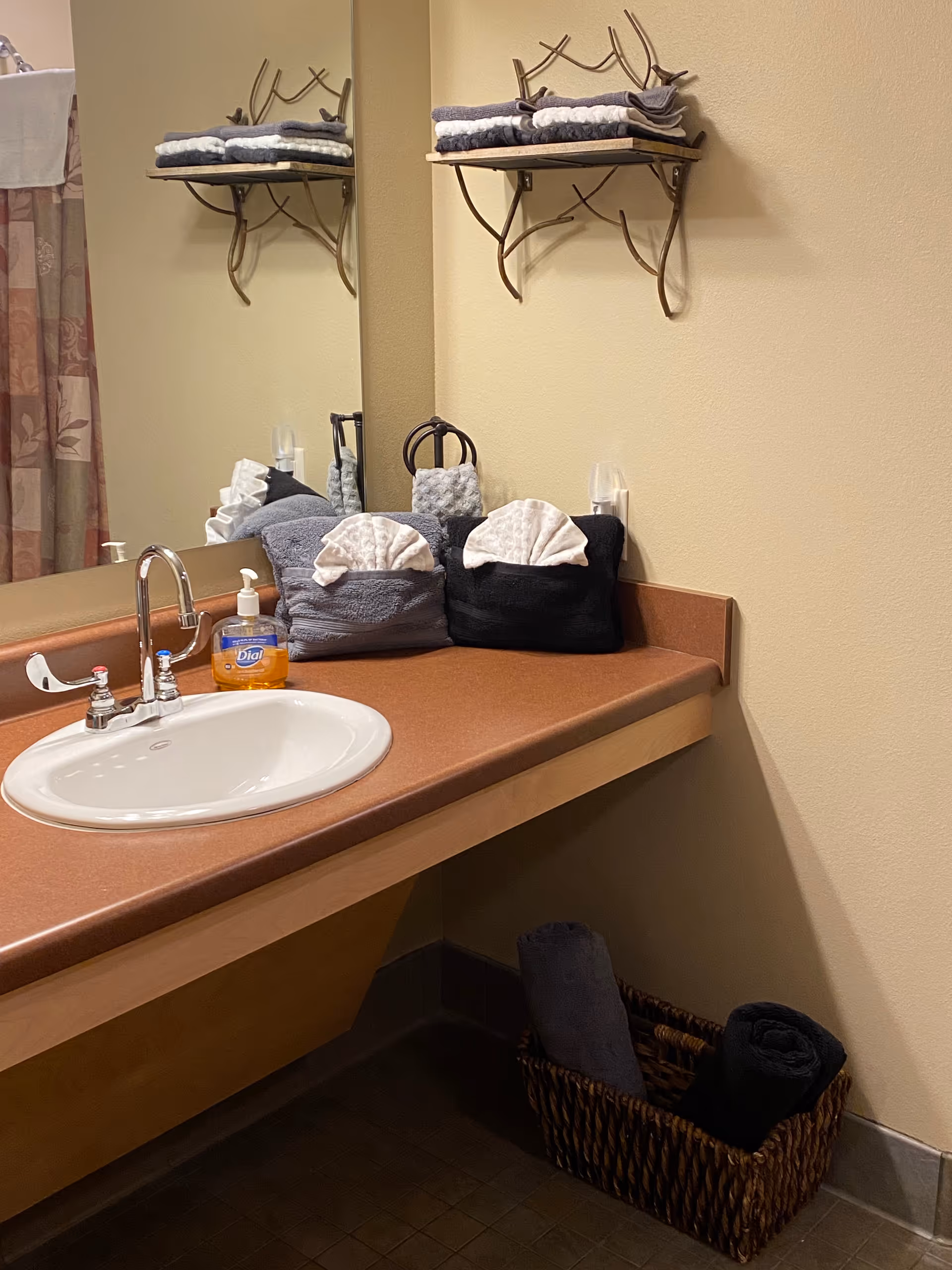 Bathroom sink with towels, shelves, mirror, and a basket of towels in a senior facility.