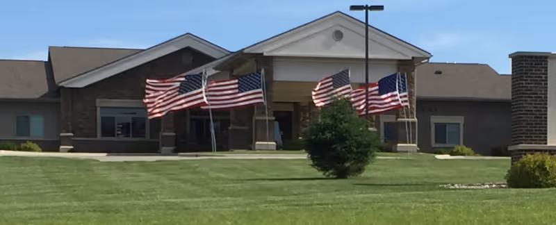 Front view of Bavarian Meadows Assisted Living with flags and a manicured lawn.