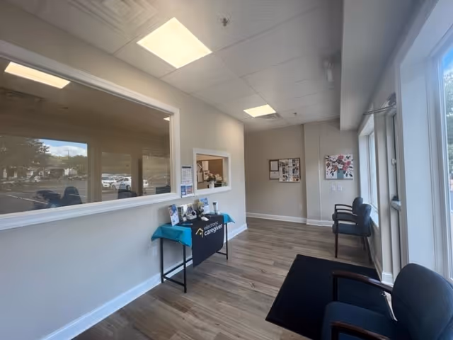 Reception area with windowed counter, teal table, bulletin boards, and seating along walls.
