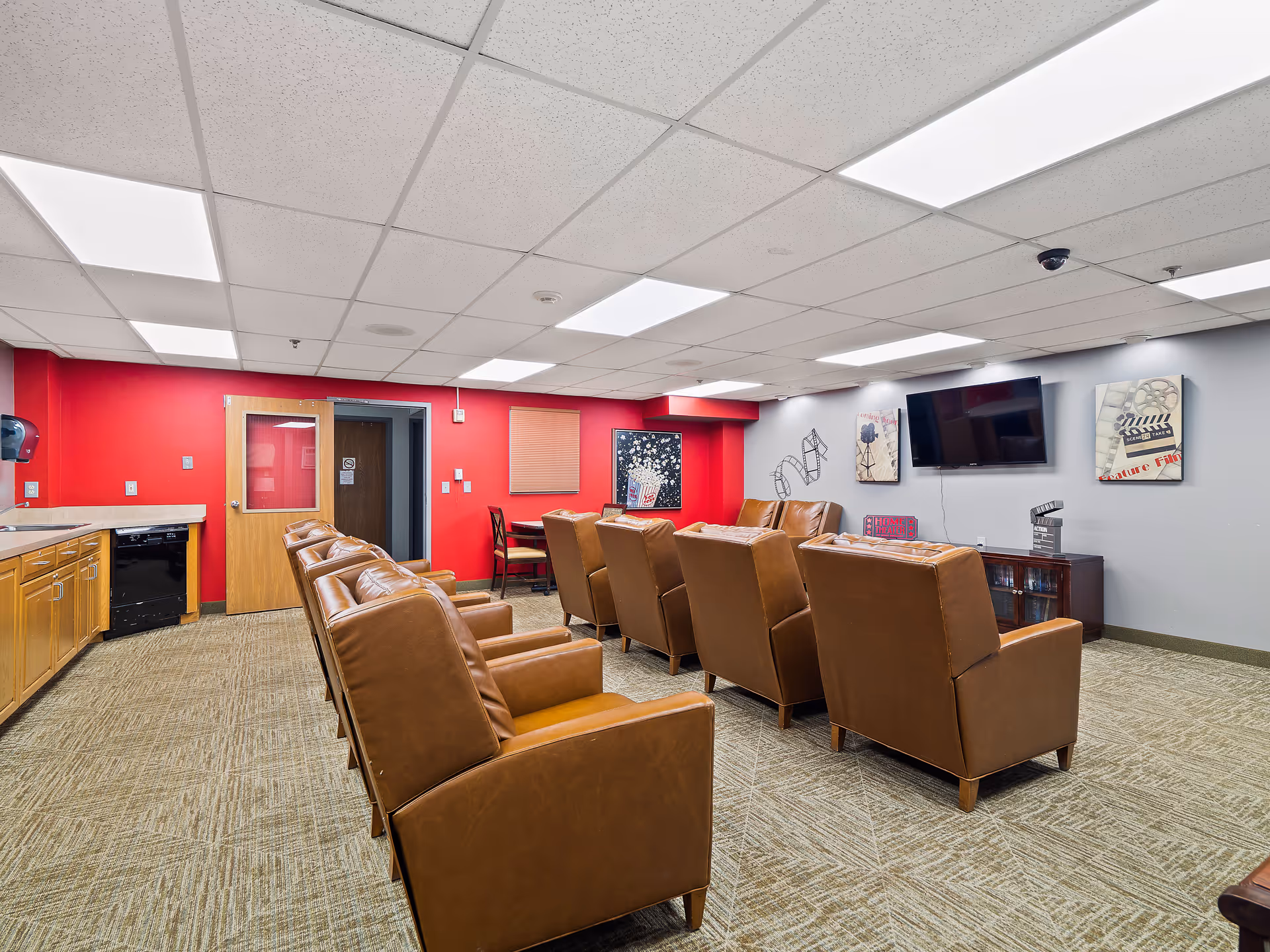 Senior living facility lounge with brown leather chairs, a wall-mounted TV, and red accent wall.