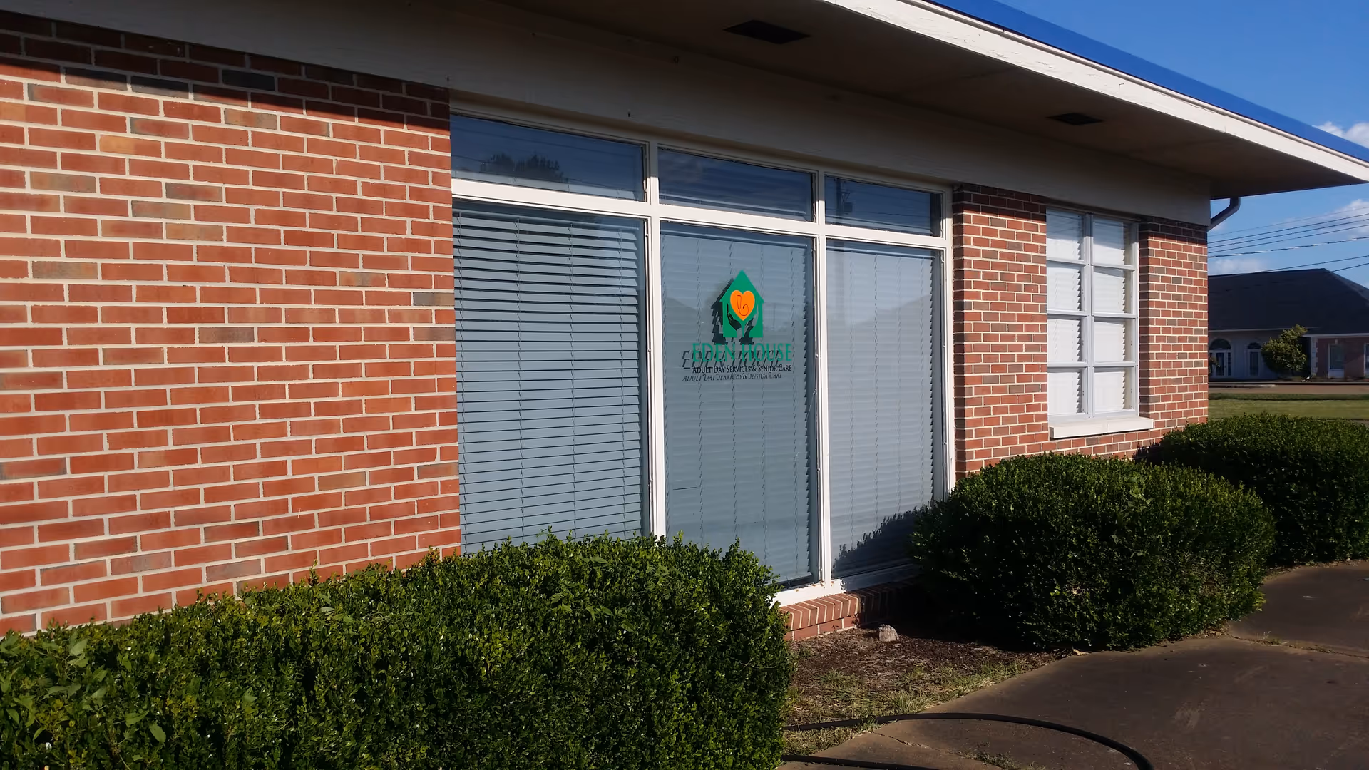 Brick senior living facility exterior with large windows and trimmed hedges along the entrance.