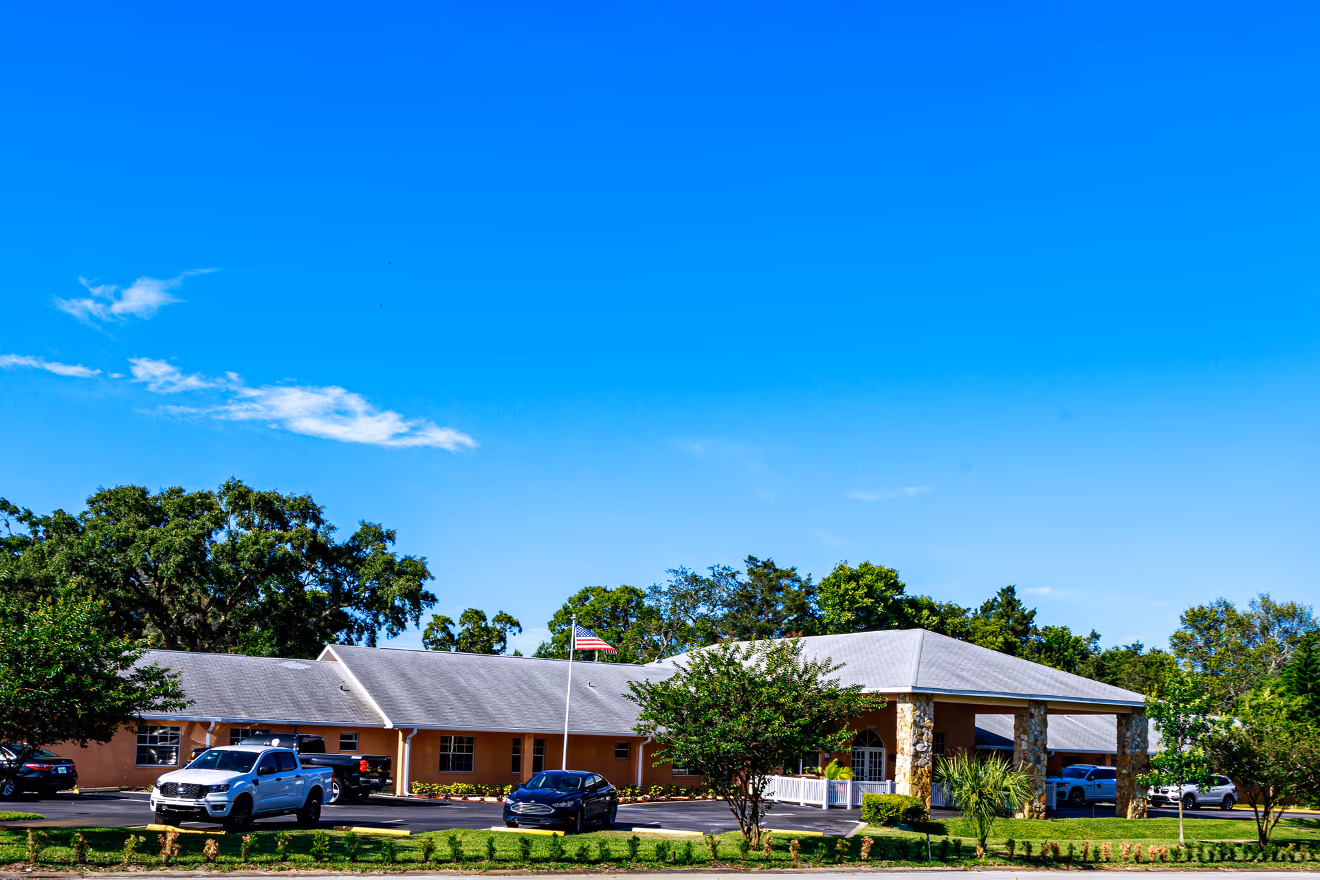 Single-story senior living facility front with parking lot and flagpole.