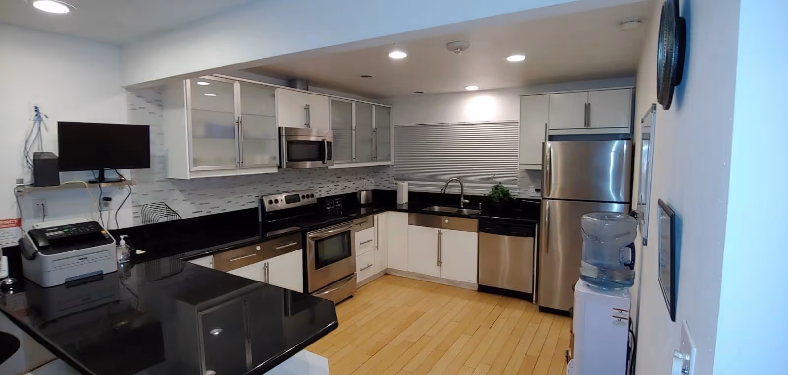 Modern kitchen with stainless appliances, black countertops, light wood floor, and water cooler.