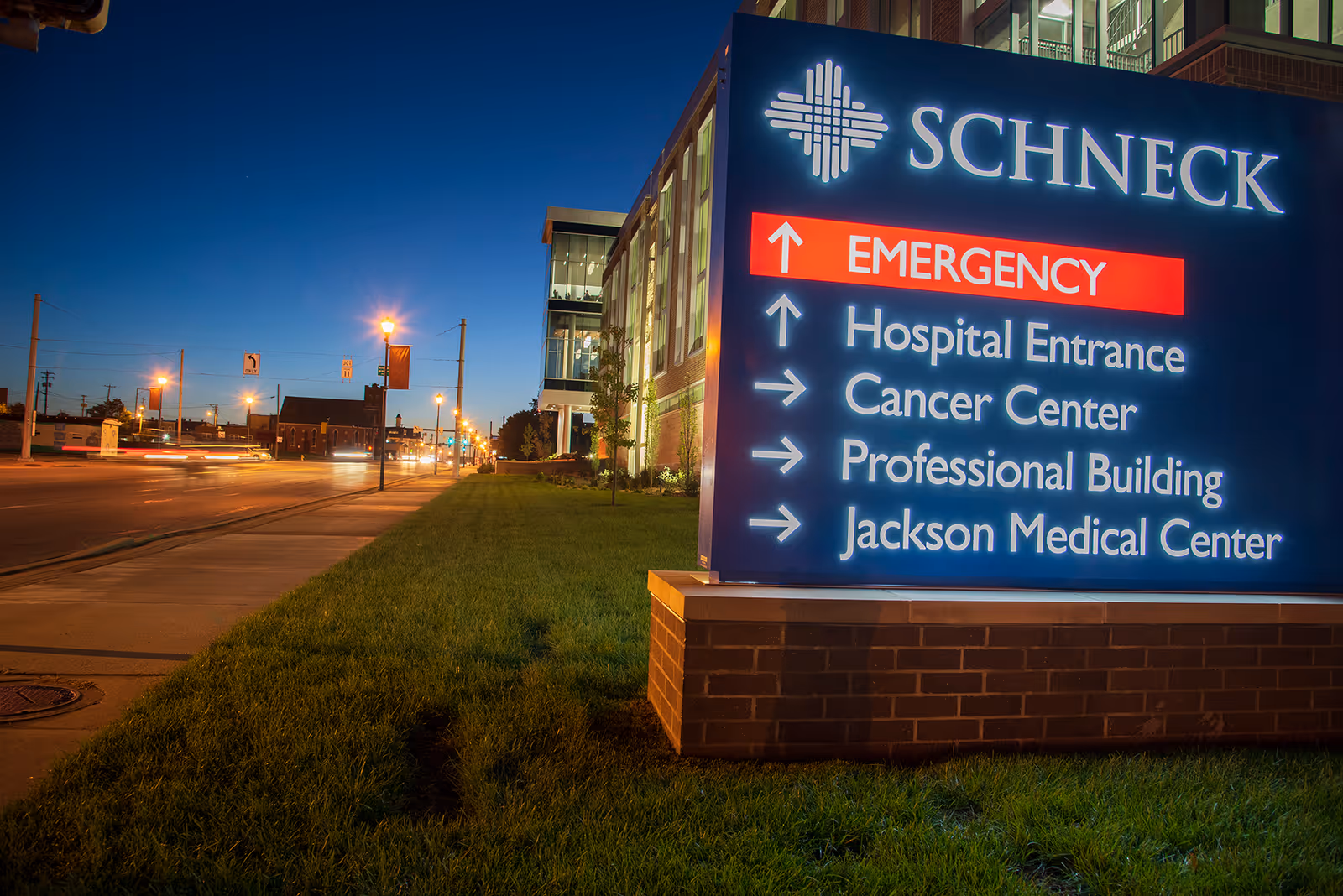 Evening exterior view of Schneck Medical Center sign with directions and street lights.