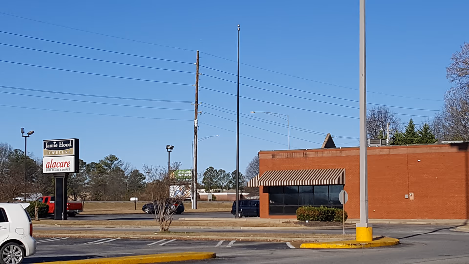 Street view of a brick commercial building with striped awning and parking lot.