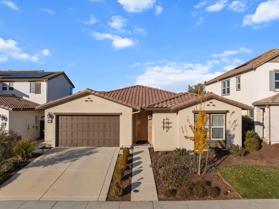 Suburban single-story beige assisted living home with brown tile roof and two-car garage.