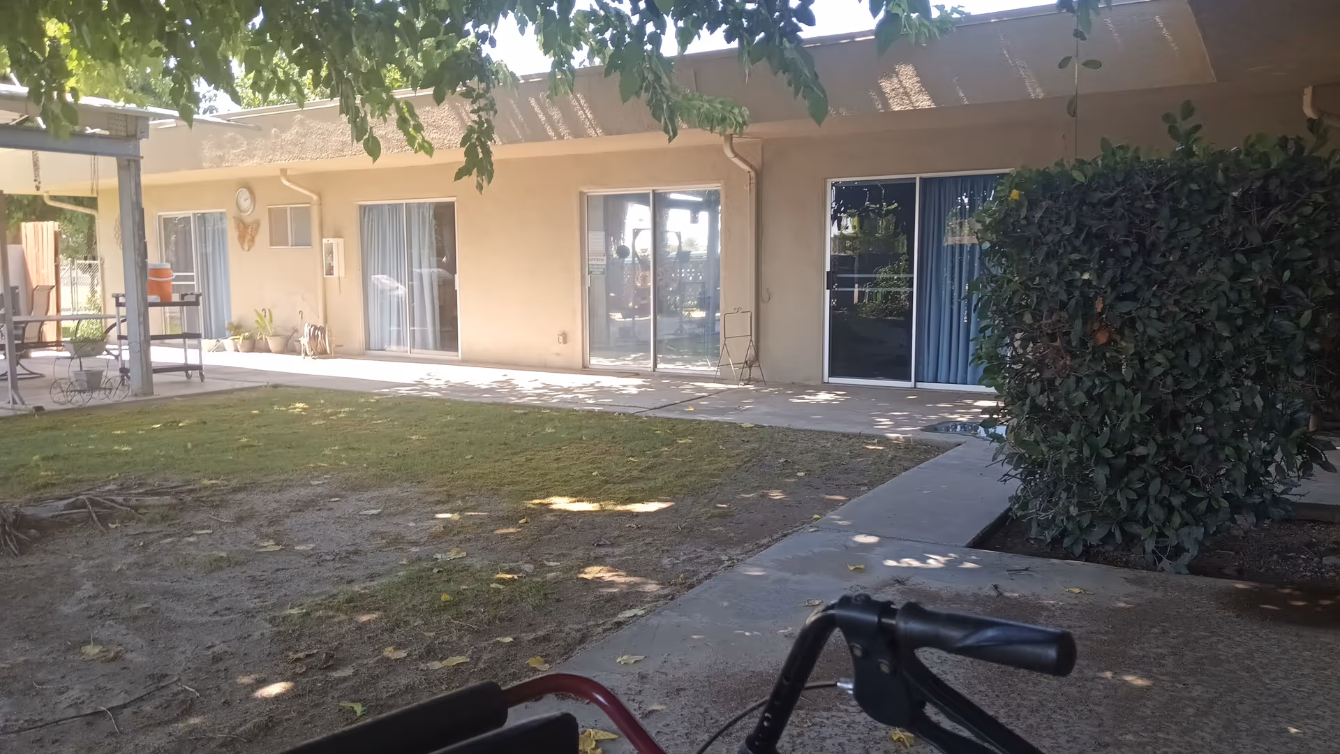Exterior view of Delano PostAcute Care outdoor courtyard with sliding doors, patio furniture, and shaded lawn.