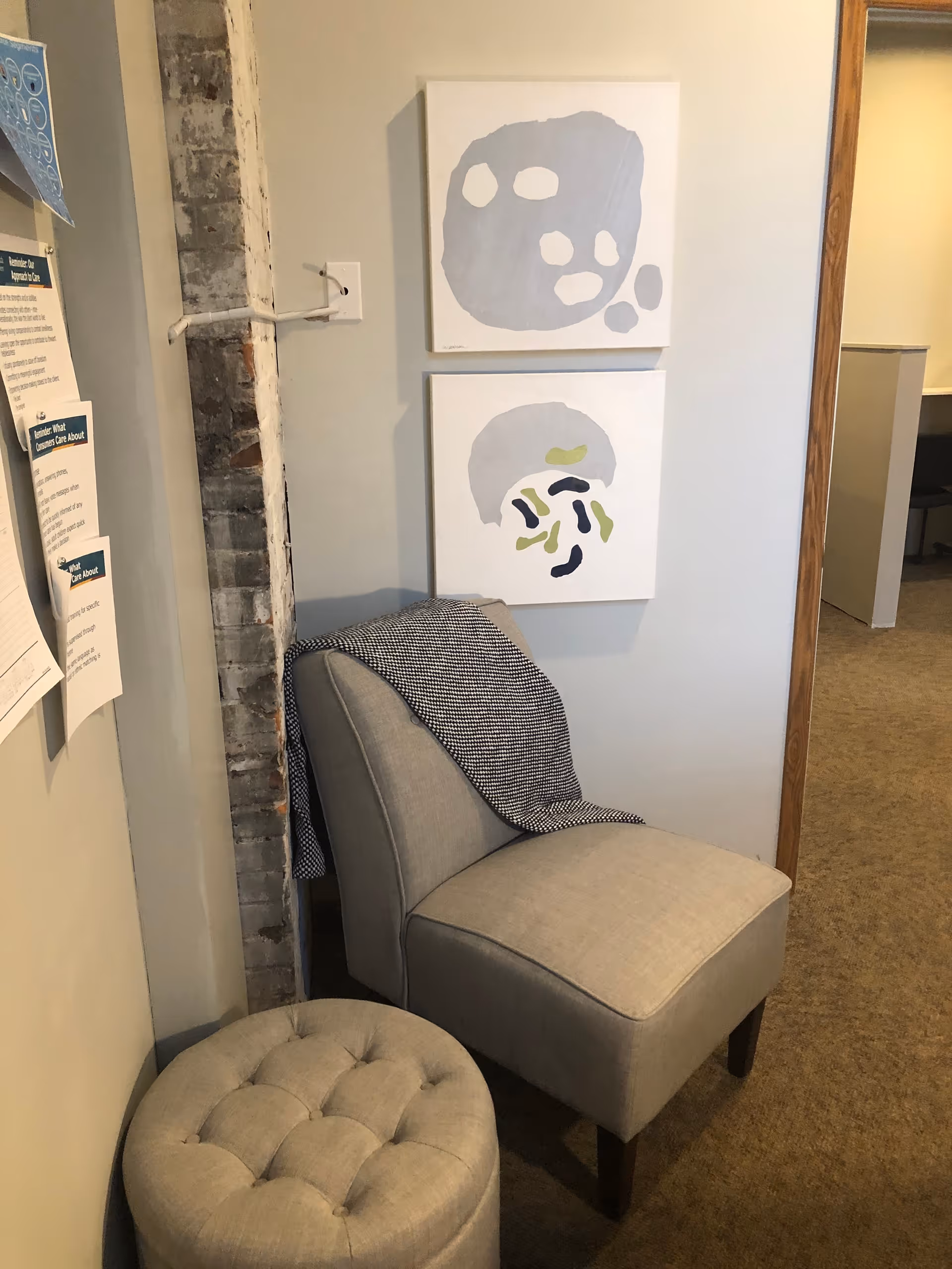 Cozy gray chair with an ottoman in a corridor seating area with abstract wall art.