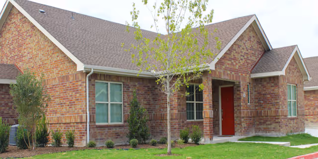 Brick exterior of Emerald Cottages of Stonebridge with a red front door and landscaped yard.