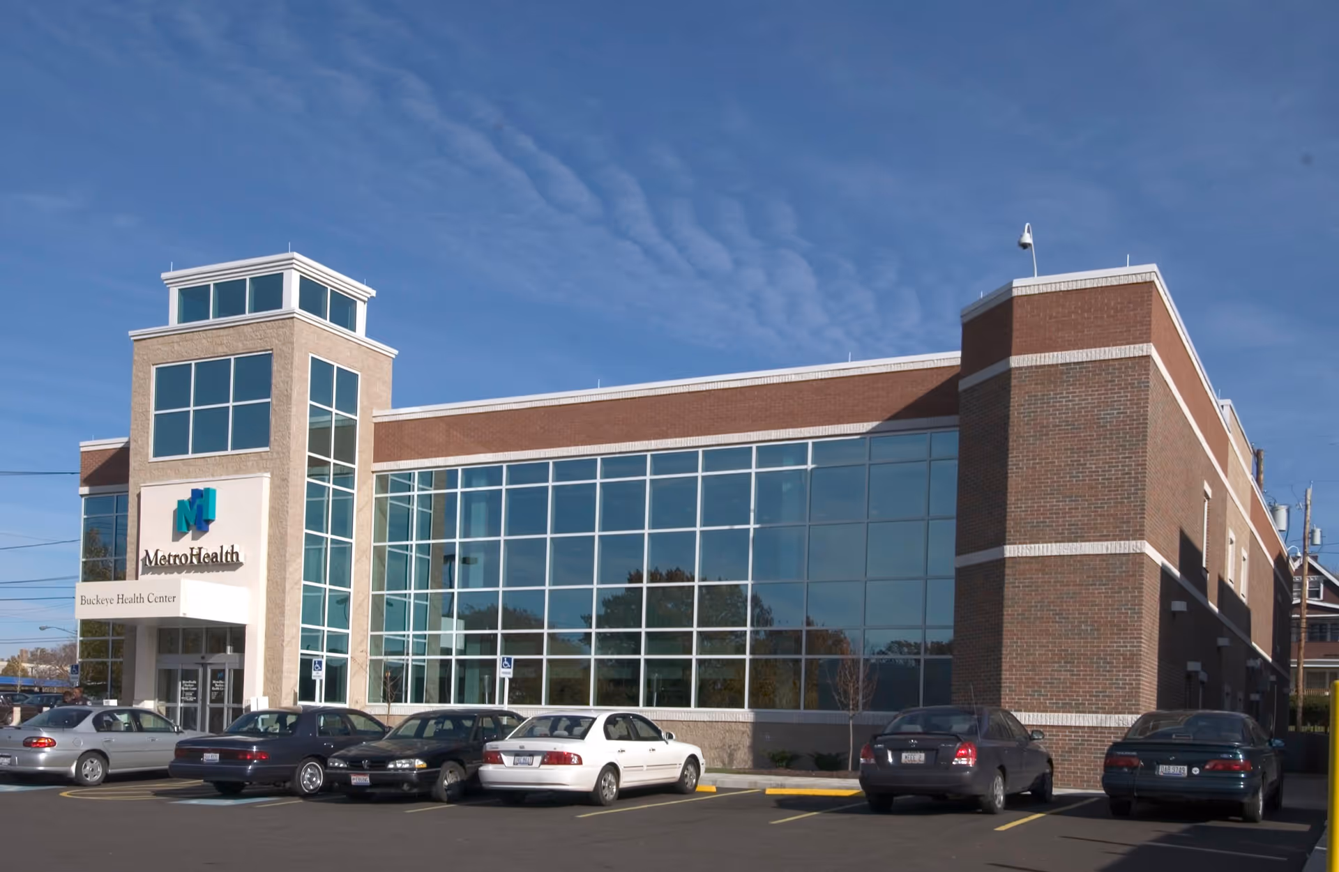Exterior view of MetroHealth Buckeye Health Center building with glass facade and parked cars.