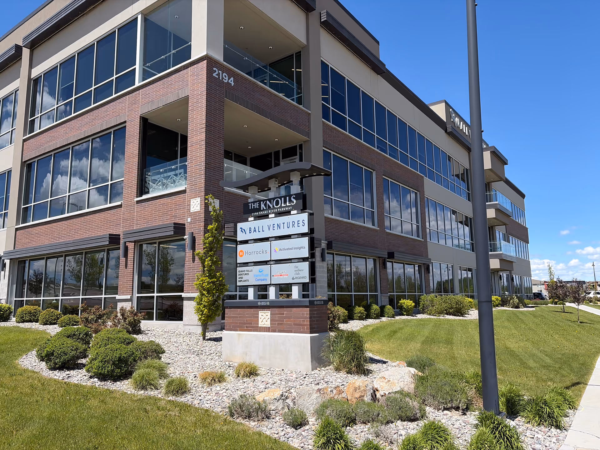 Modern three-story brick and glass senior living building with landscaped front and blue sky.