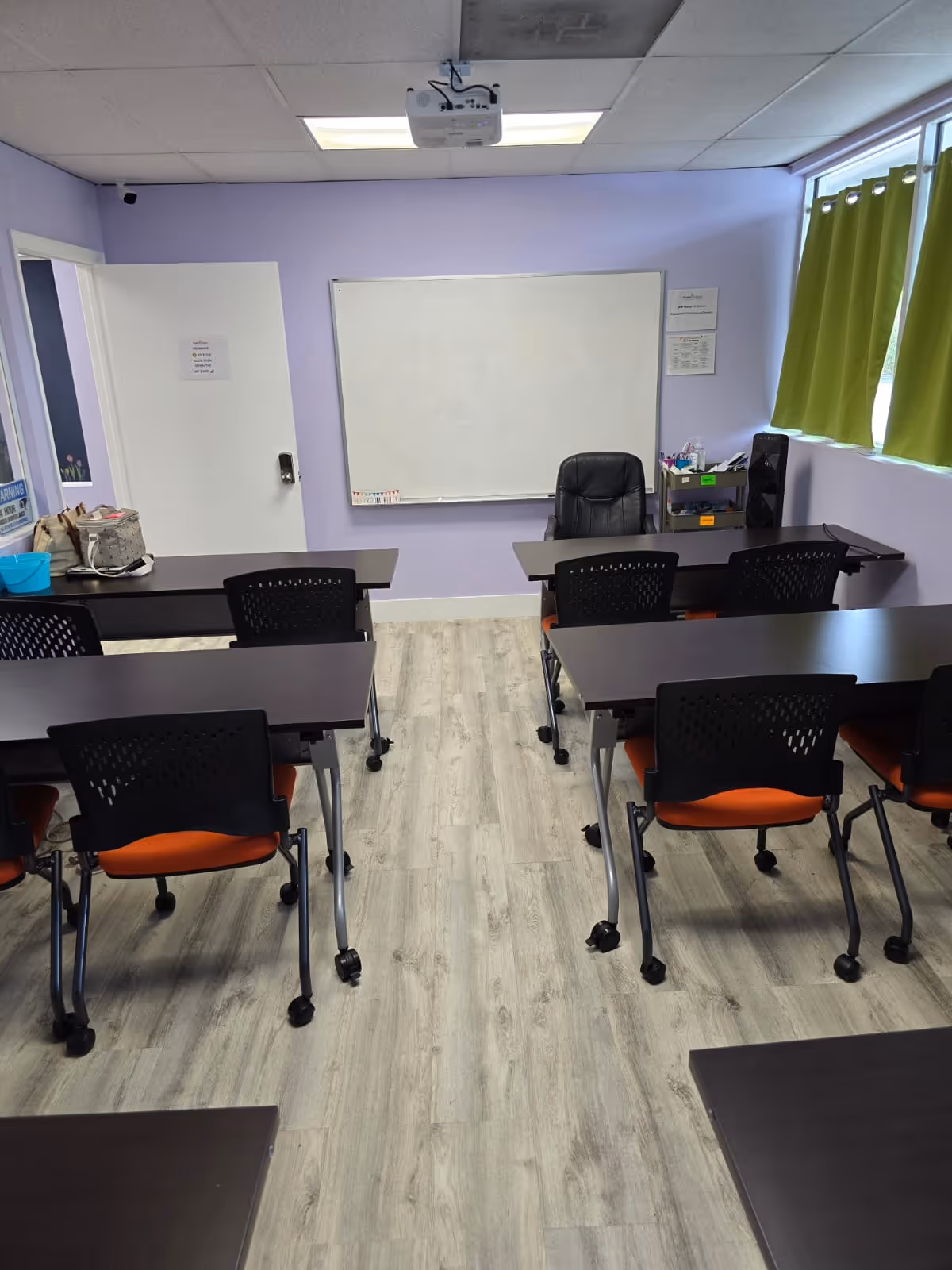 Purple-walled classroom with whiteboard, projector, and rows of desks and orange chairs.