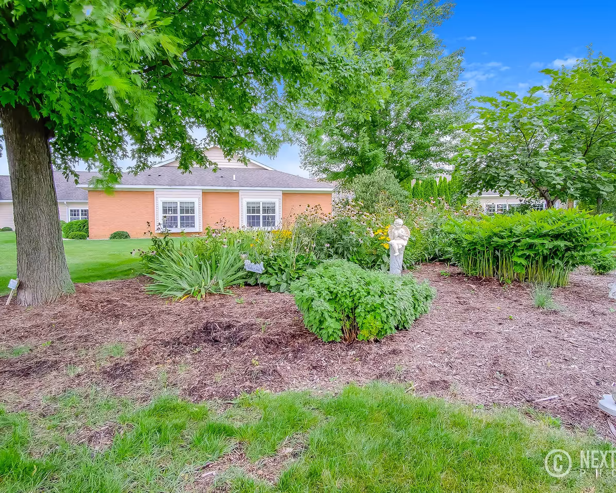 Lush garden with shrubs and a statue in front of a brick building exterior.